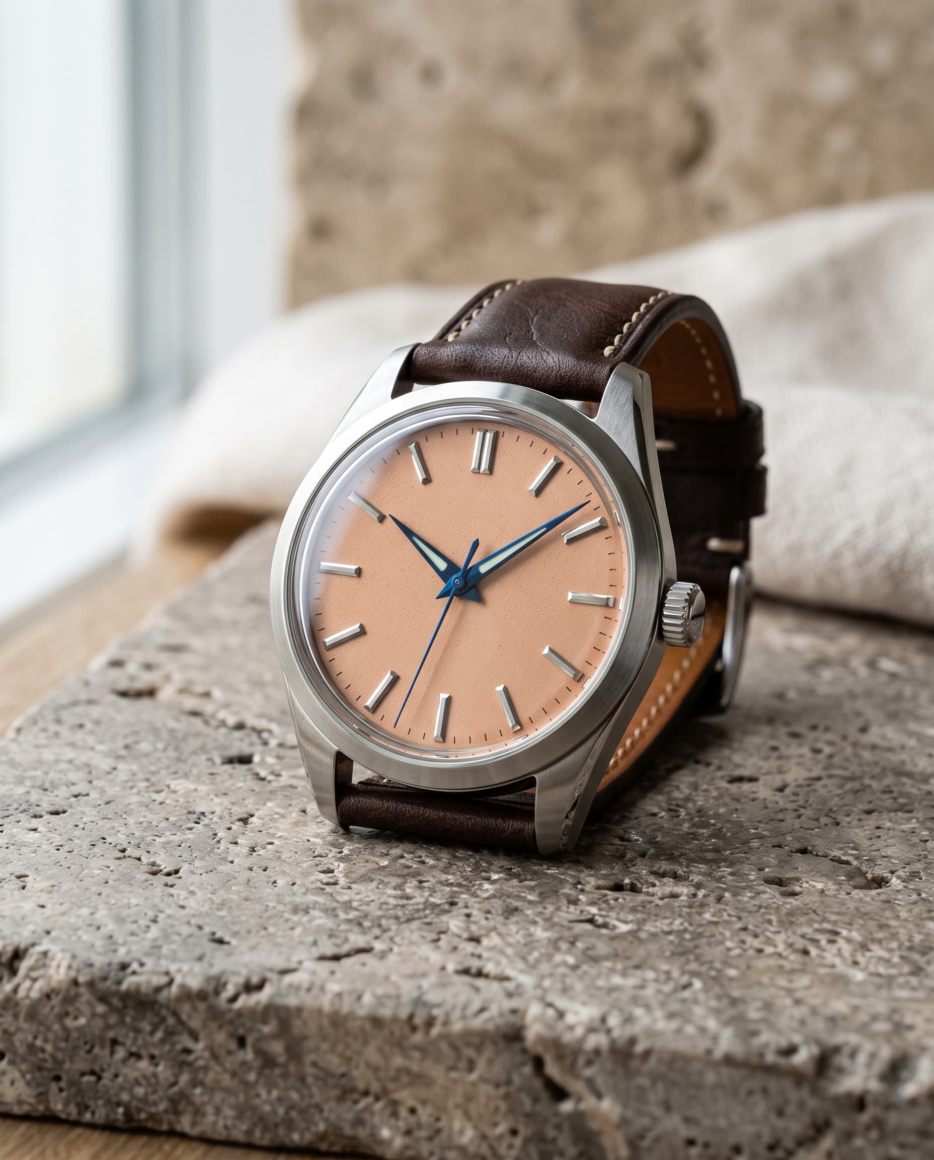 A steel watch with a salmon dial, steel baton indices and blued hands on a dark brown leather strap.